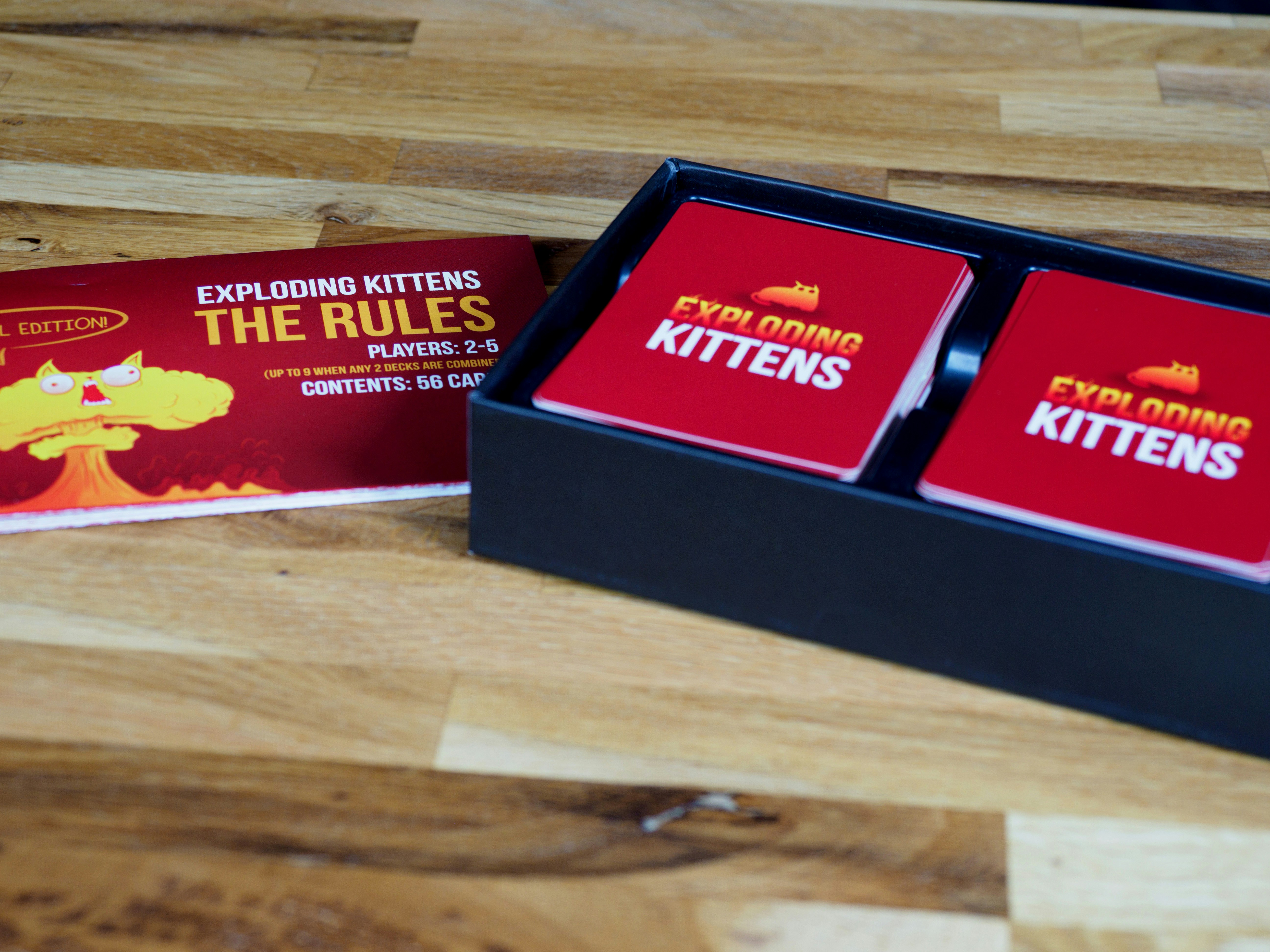 An open Exploding Kittens card game box sits on a table with the instructions to the left.
