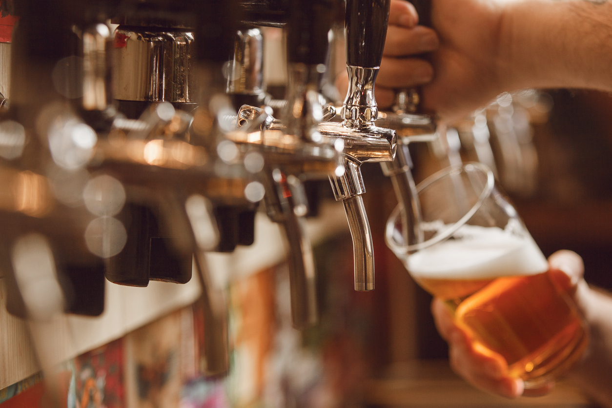 A bartender fills a glass with seasonal beer from the tap in a bar during the evening.