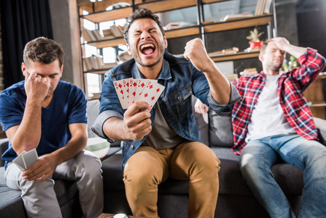 One man sits in between his friends, screaming excitedly that he won a card game.